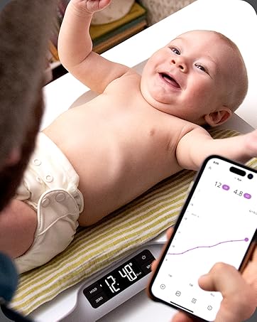 Baby being weighed on scale with father holding phone in the foreground