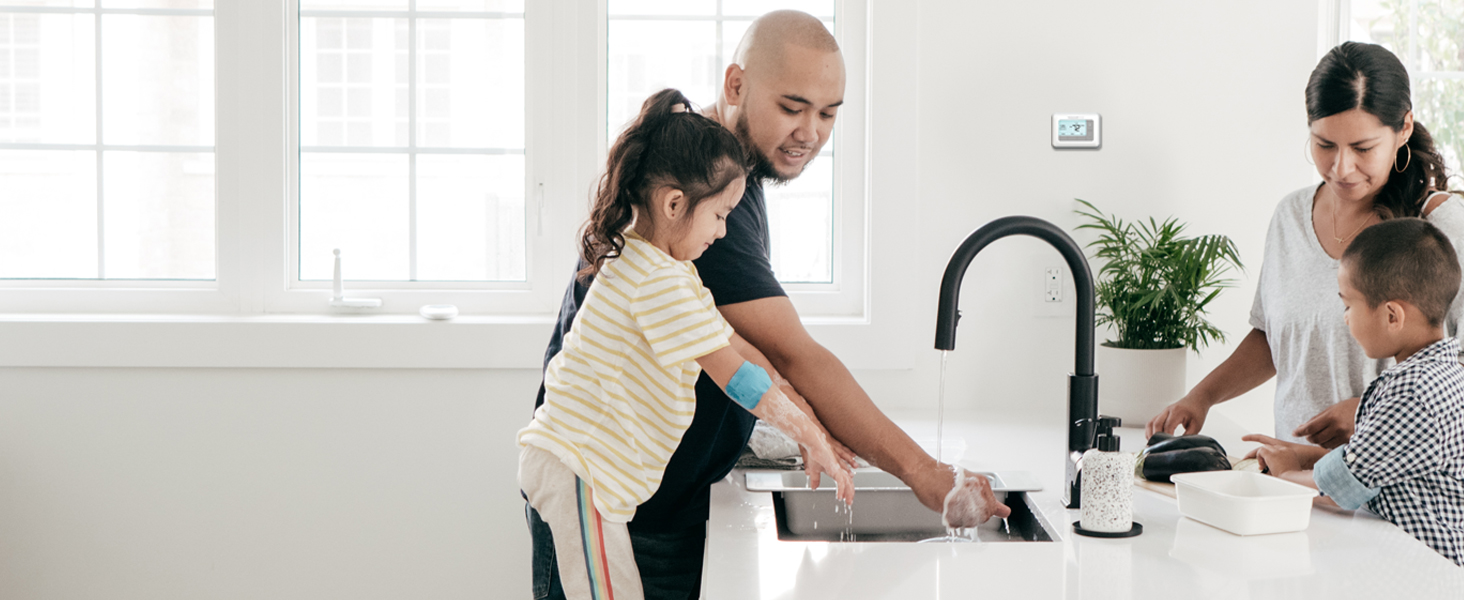 Two parents and two children washing the dishes with a thermostat on the wall behind them.