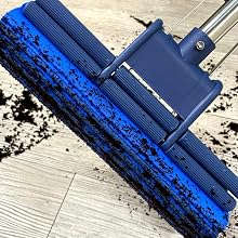 Blue floor mop with wide rectangular head and long handle. Demonstrated cleaning dirt from light-colored wooden floor.