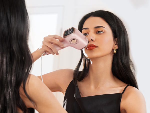 Woman using a pink handheld device with a round head on her face. The device appears to be an electronic beauty tool for facial treatment.