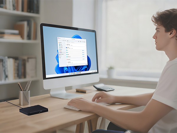 Person working at desk setup with computer monitors displaying interface screens, shown from multiple angles in well-lit office environment.