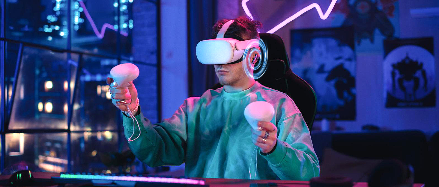Person wearing white VR headset and headphones, holding pink controllers in neon-lit environment. Demonstrates virtual reality gaming or interactive experience.