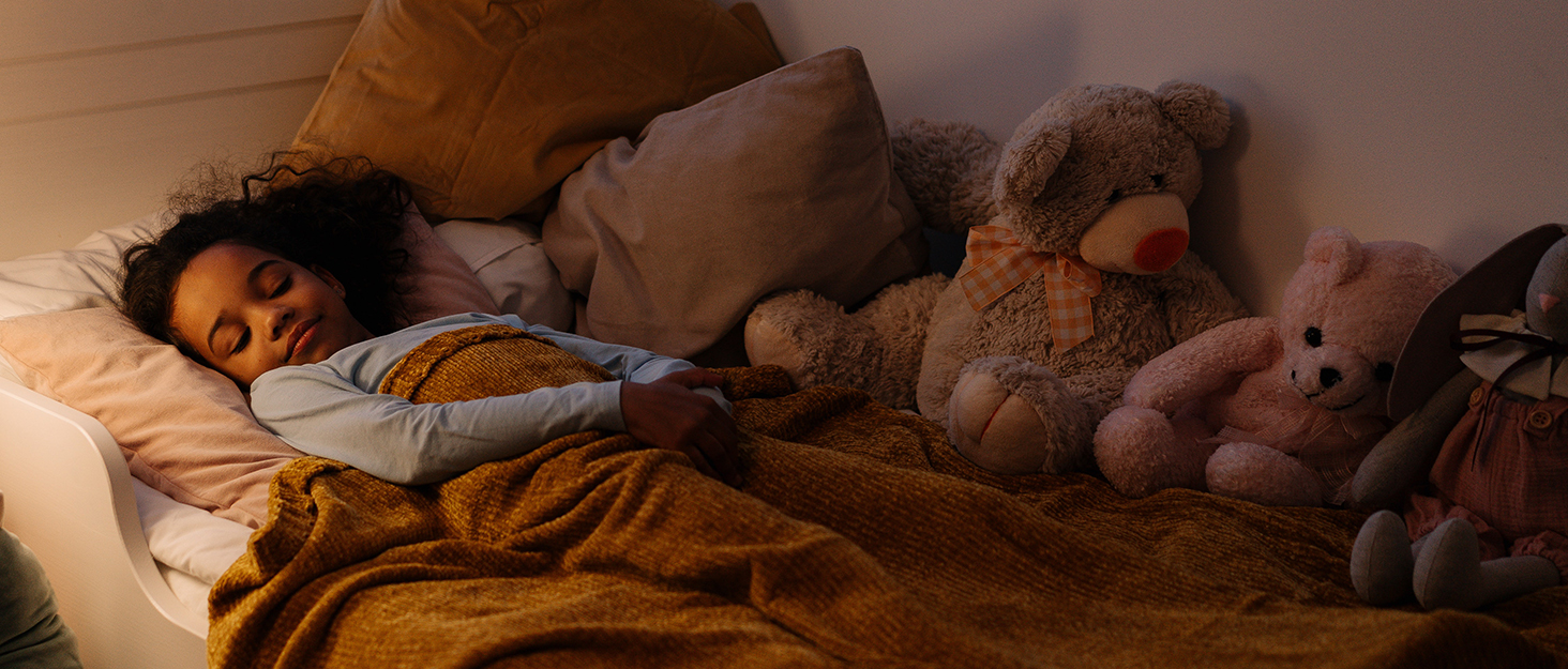 a child sleeping on a bed with a teddy bear.