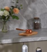 Kitchen countertop with marble surface. Blurred vase with flowers, glass container, and wooden board with honey dipper in background. Two metal canisters in foreground.