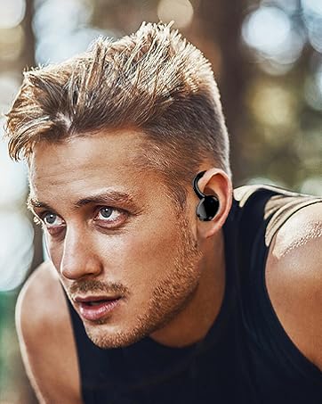 Close-up of a man with short blond hair wearing a black tank top and a wireless earbud in his ear.
