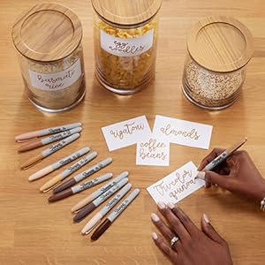 Person writing with Sharpie Portrait Markers and additional markers on table