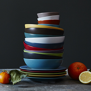 A stack of dinnerware in Colorwave, in varying colors, on a metal surface with a dark background.