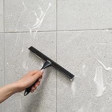 Black shower squeegee wipes the bathroom tiles