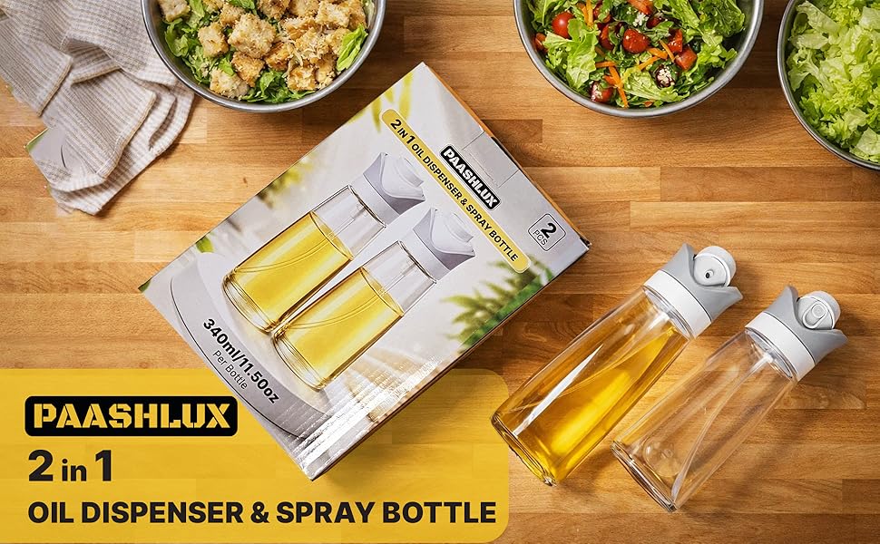 Two clear oil dispensers and their packaging are on a wooden table, surrounded by bowls of salad.