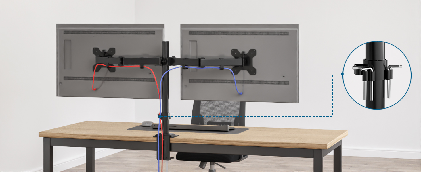 Dual monitor arm mount attached to a wooden desk. Black metal construction with adjustable arms and cable management features. Close-up of mounting mechanism.