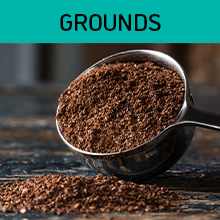 A scoop of ground coffee next to a pile of ground coffee on a wood table