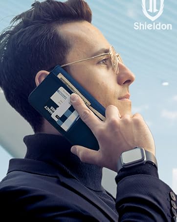 Smartphone case designed to resemble a floppy disk, held to ear. User wears gold-rimmed glasses and dark jacket. Smartwatch visible on wrist. 'Shieldon' logo in corner.