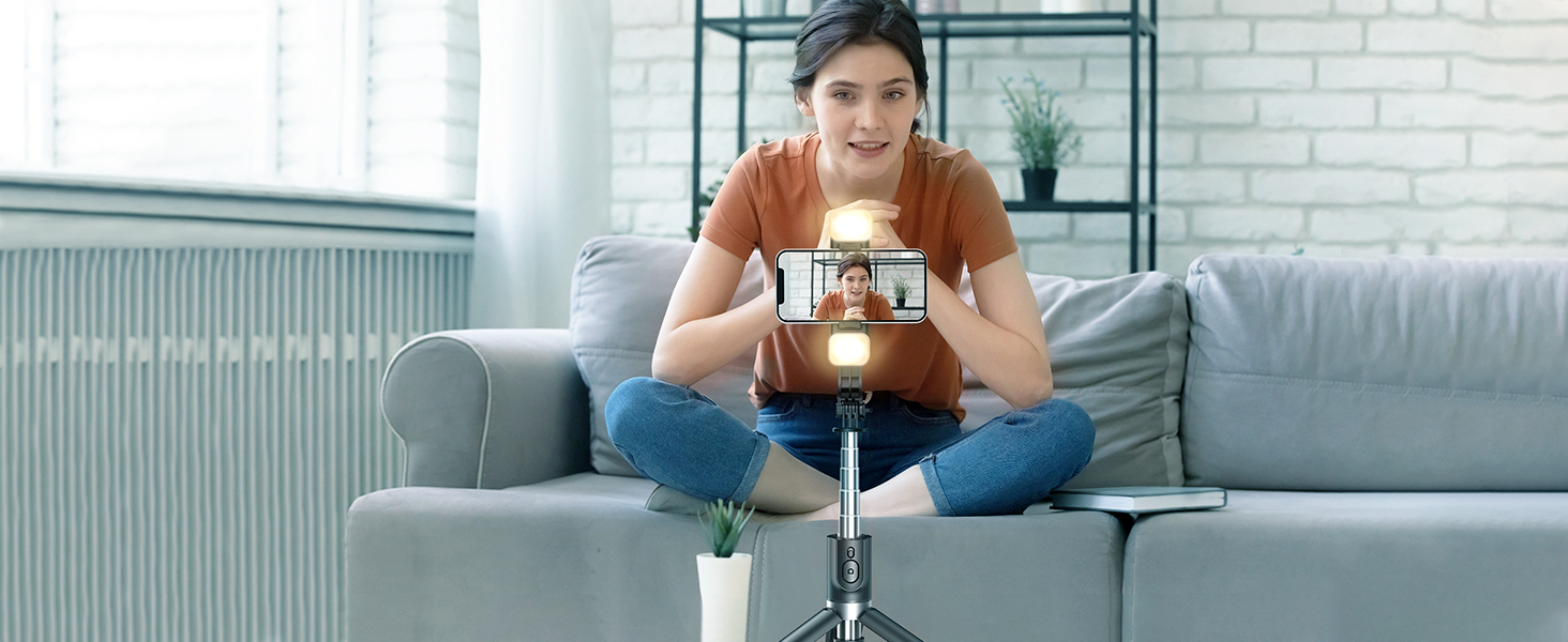 a woman sits on a couch, taking a self portrait with her phone.