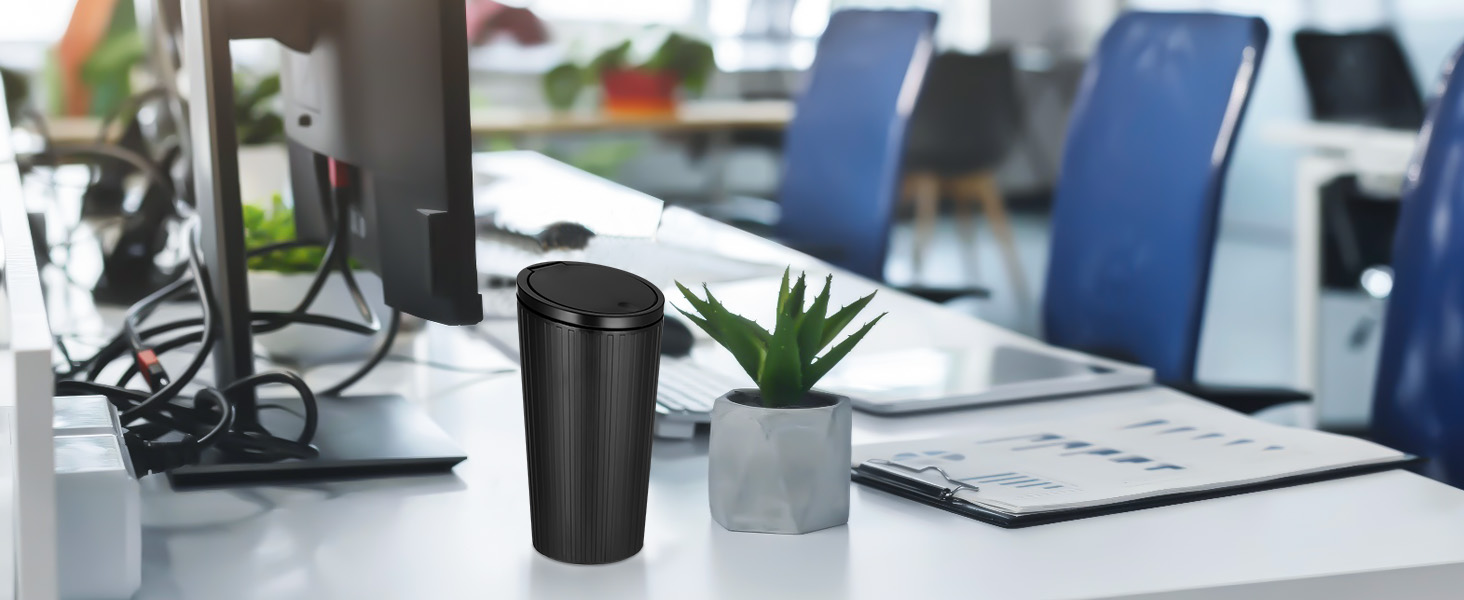Modern office desk setup with black computer monitor, black cylindrical speaker or container, and small potted succulent plant on white desktop.