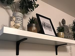 White floating shelf on a wall, decorated with various items including a framed 'Home' sign, plants, and decorative objects.