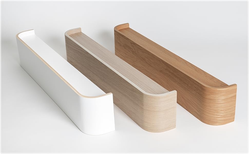 Three minimalist wooden wall shelves in white, light wood, and dark wood finishes. Each shelf has a sleek, L-shaped design with a raised edge.