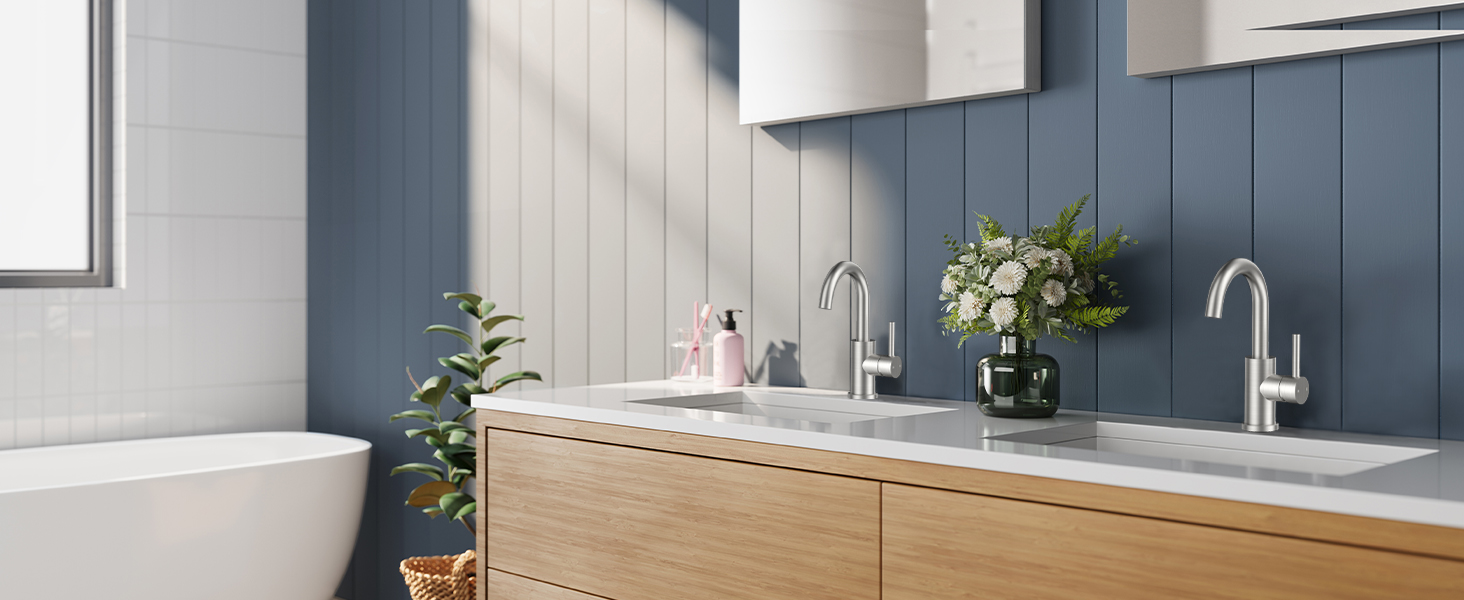 Modern bathroom featuring light wood vanity with white countertop, blue wall panels, and white cabinets. Stainless steel faucets and green plants add accents.
