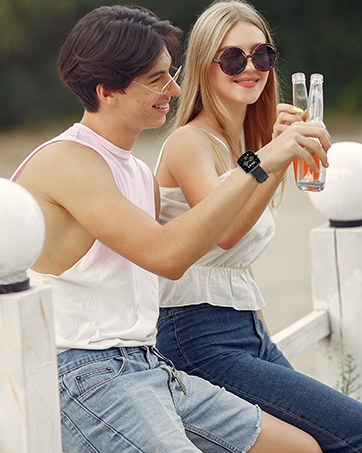 Two people sitting outdoors, holding glasses with beverages. One person wearing sunglasses and a smartwatch, both in casual summer attire.