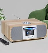 Compact digital radio or music system with silver-gray housing and display screen, placed on light surface with plant decoration in background.