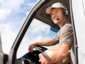 Person wearing a headset and cap, sitting in the driver's seat of a vehicle, looking out the window with a smile.