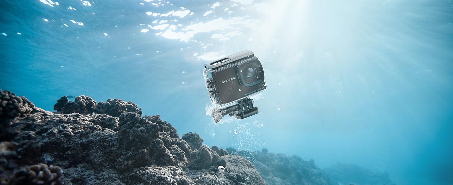 Compact action camera underwater, capturing coral reef scene. Device appears waterproof, with rectangular shape and lens visible. Sunlight filters through water above.