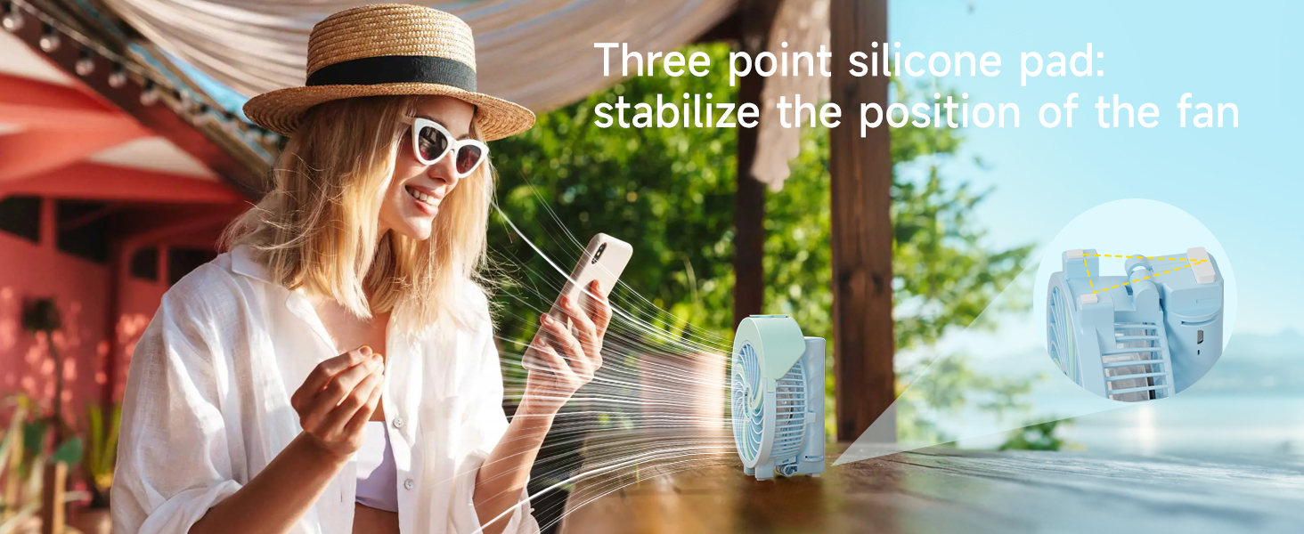Portable fan with three-point silicone pad for stability. Woman using smartphone outdoors with fan nearby, demonstrating its use in a sunny setting.