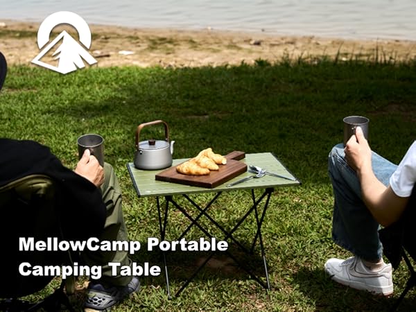 Adults enjoy lakeside picnic with a portable foldable camping table holding croissants and teapot
