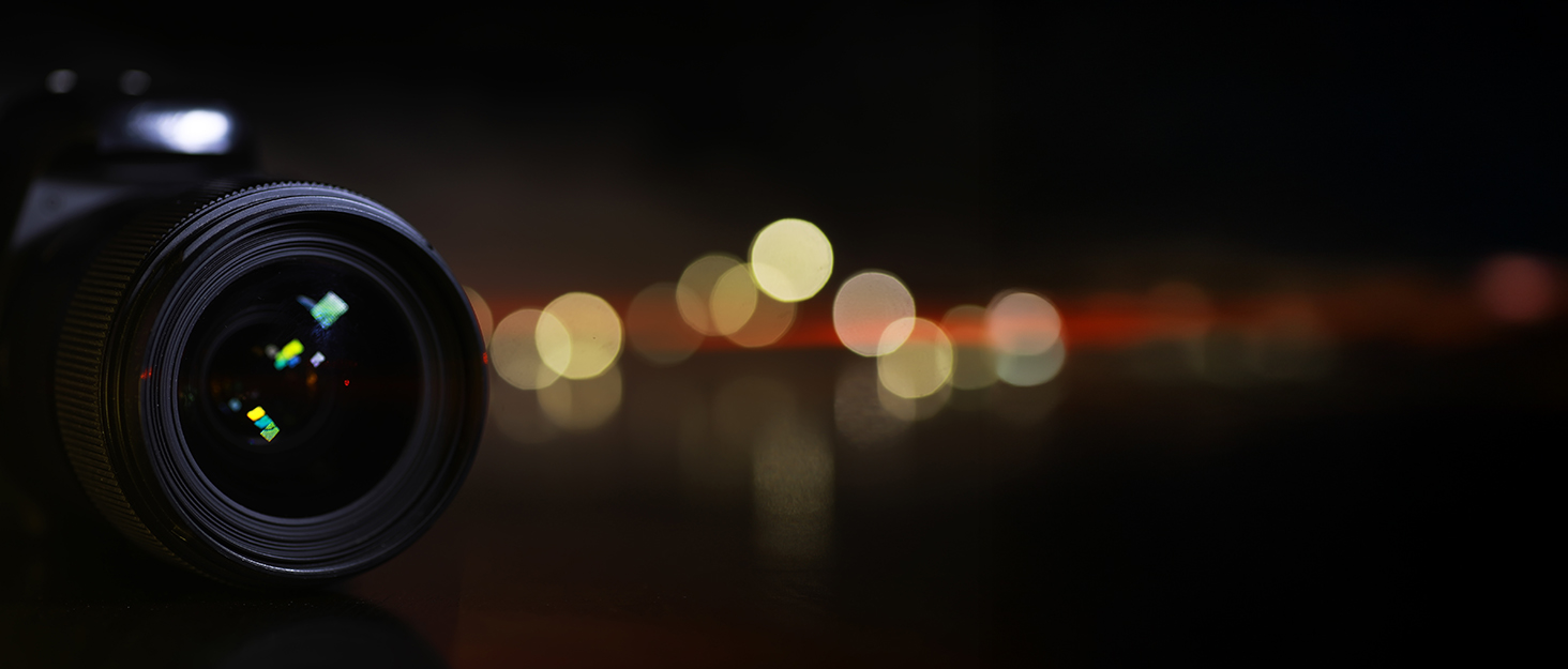 Abstract dark background with circular bokeh light effects and lens elements, suggesting professional photography or optical equipment.