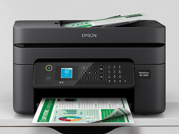 Black WorkForce WF-2930 sitting on cabinet with prints in output tray.