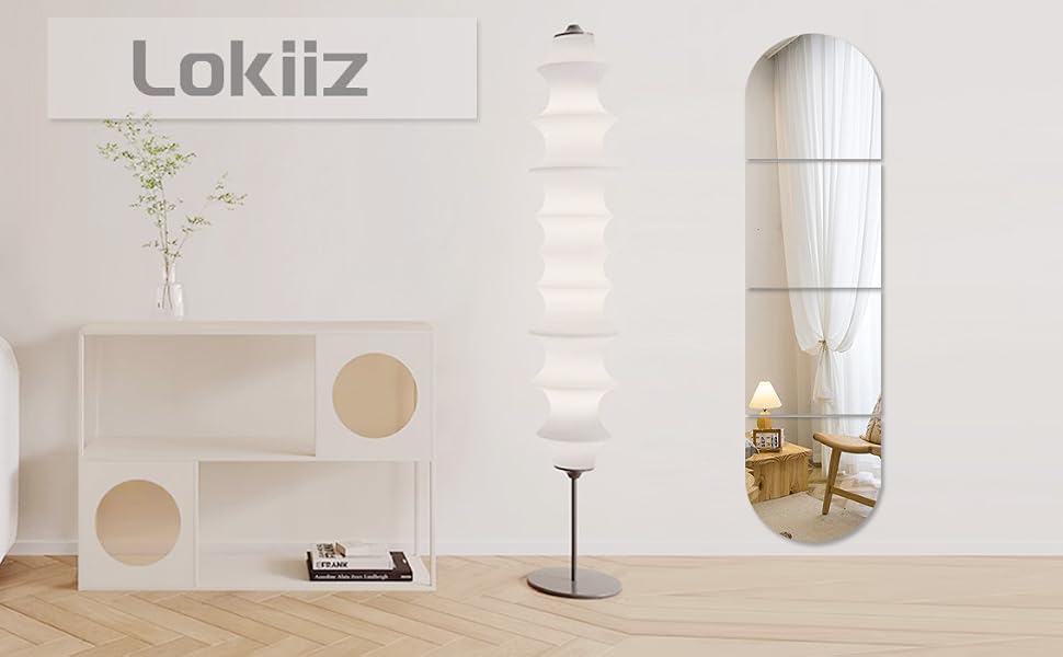 Minimalist interior with white walls, featuring a geometric wood structure with circular cutouts, arched mirror, floor lamp, and potted plant.