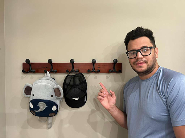 A man is very happy that this coat rack holds his backpack and hat.