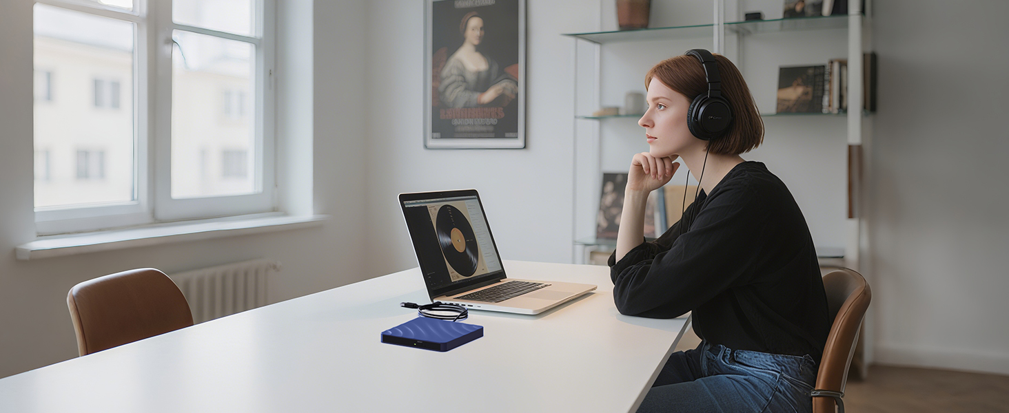 Person working with laptop and phone in bright room with window.