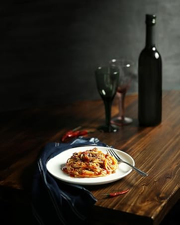 Plate of pasta dish on wooden table with wine bottle, glasses, and moody lighting, creating a restaurant-like ambiance.