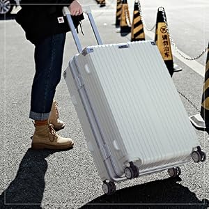 Large white hardshell suitcase with ribbed exterior and wheels. Person pulling luggage on street, demonstrating its use for travel.