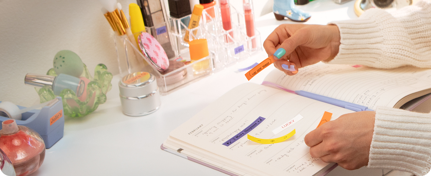 Person applying Brother P-touch Btag reminder and inspiration labels to planner notebook on desk