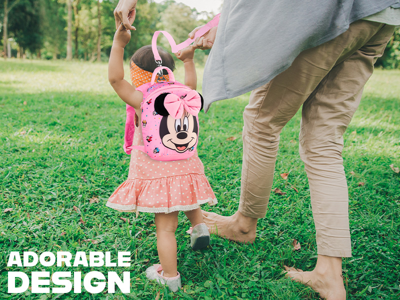 Pink Minnie Mouse backpack worn by child in orange dress. Adult holds child's hand in outdoor setting. Text overlay reads 'ADORABLE DESIGN'.