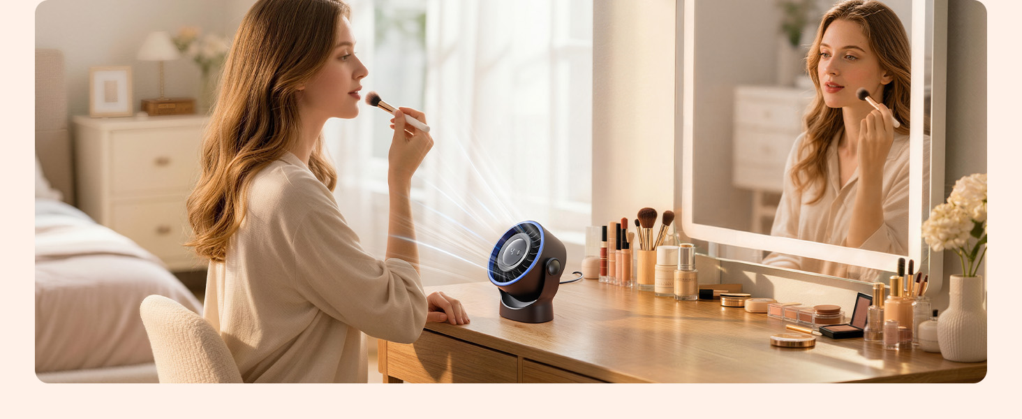 Person applying makeup at vanity table with mirror, surrounded by beauty products and a round speaker or device on desk in warm-lit bedroom setting.