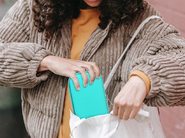 Hands placing a turquoise wallet or small item into a white shopping bag while wearing a chunky knit beige sweater.