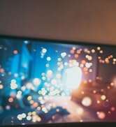 Blurred image showing colorful bokeh lights in blue, orange, and yellow tones, creating a festive or celebratory atmosphere.