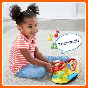 Kid pretends to drive, turning the steering wheel. Toy plays music and says: Toot-Toot!