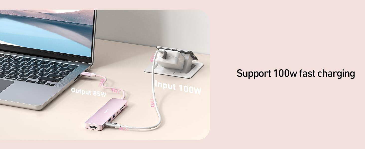 USB-C charger connected to laptop and pink portable battery pack. Text indicates support for 100W fast charging. Charger has metallic finish and compact design.