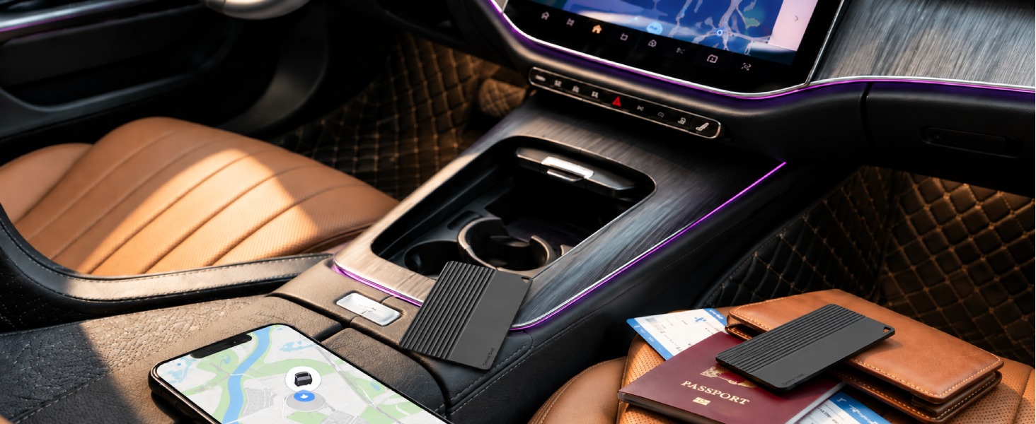 Slim tracker card, black, placed inside a car with a passport, wallet and smartphone.