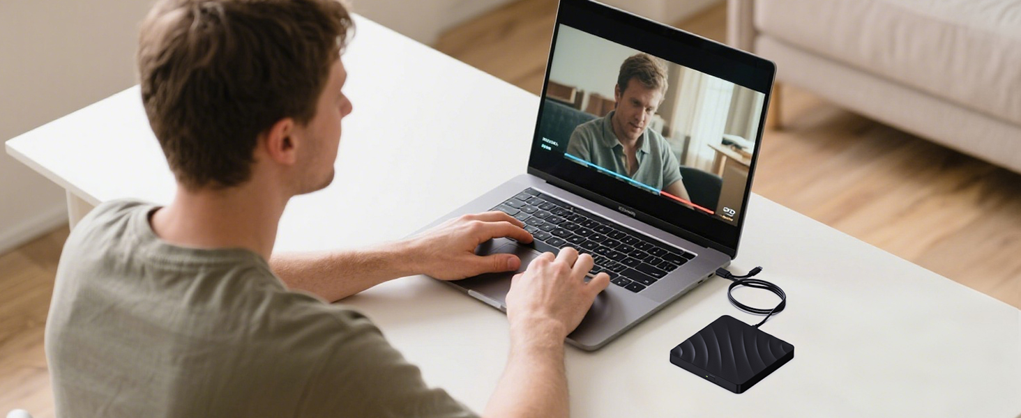 Person at desk participating in video call on laptop with external microphone visible in foreground. Shows home office setup in natural lighting.