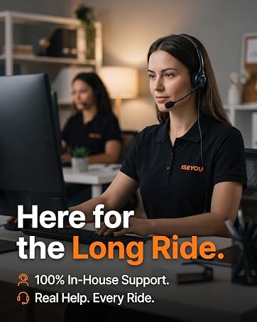 Text reads 'Here for the Long Ride.' followed by '100% In-House Support.' and 'Real Help. Every Ride.' Woman wearing black branded shirt in office environment with colleague blurred in background.