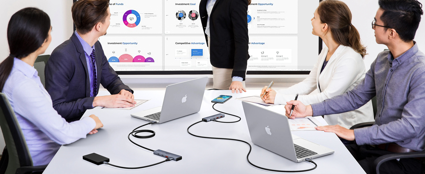Business meeting scene with people seated around a table viewing presentation materials, with laptops present.