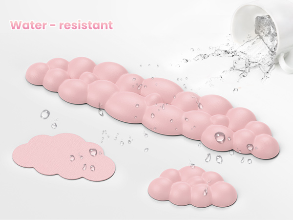 Water-resistant pink cloud-shaped bath mats. Shown with water droplets on surface and splashing water, demonstrating their water-repellent properties.