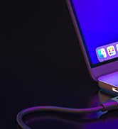 Close-up of a device corner showing a purple cable connected to a port. Blue screen visible with white app icons.