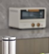 Stainless steel travel mug with lid in foreground. Blurred retro-style radio visible in background on counter.