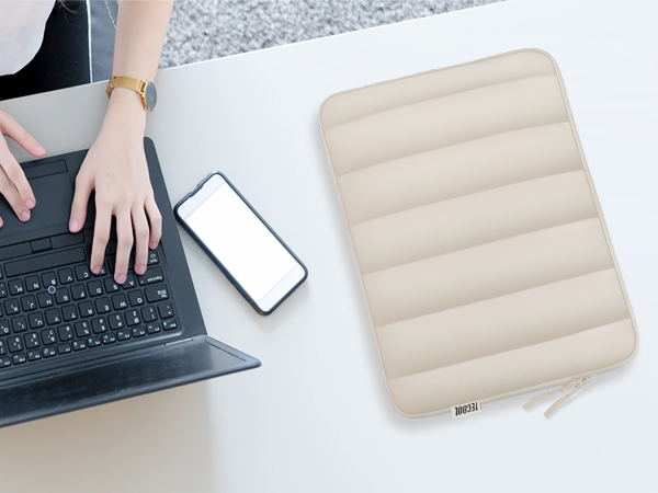 Workspace scene with laptop, smartphone, and beige padded sleeve or case on white desk surface.
