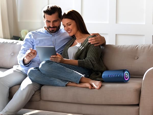 Interior scene showing two people relaxing on a grey sofa, engaging with digital devices in a well-lit living room setting.